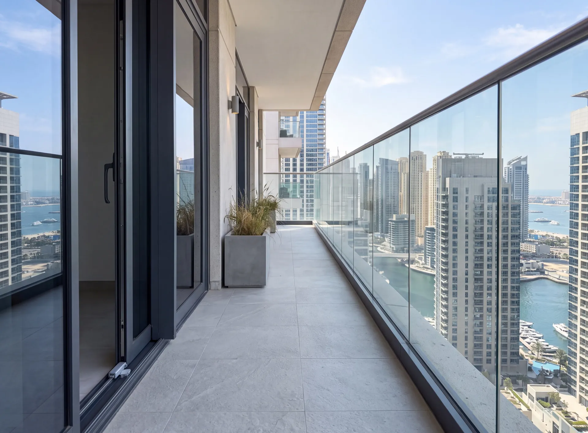 Balcony of a Dubai apartment with a full-height glass balustrade with no horizontal rails, a restrictor on the door sash and a planter set back from the edge