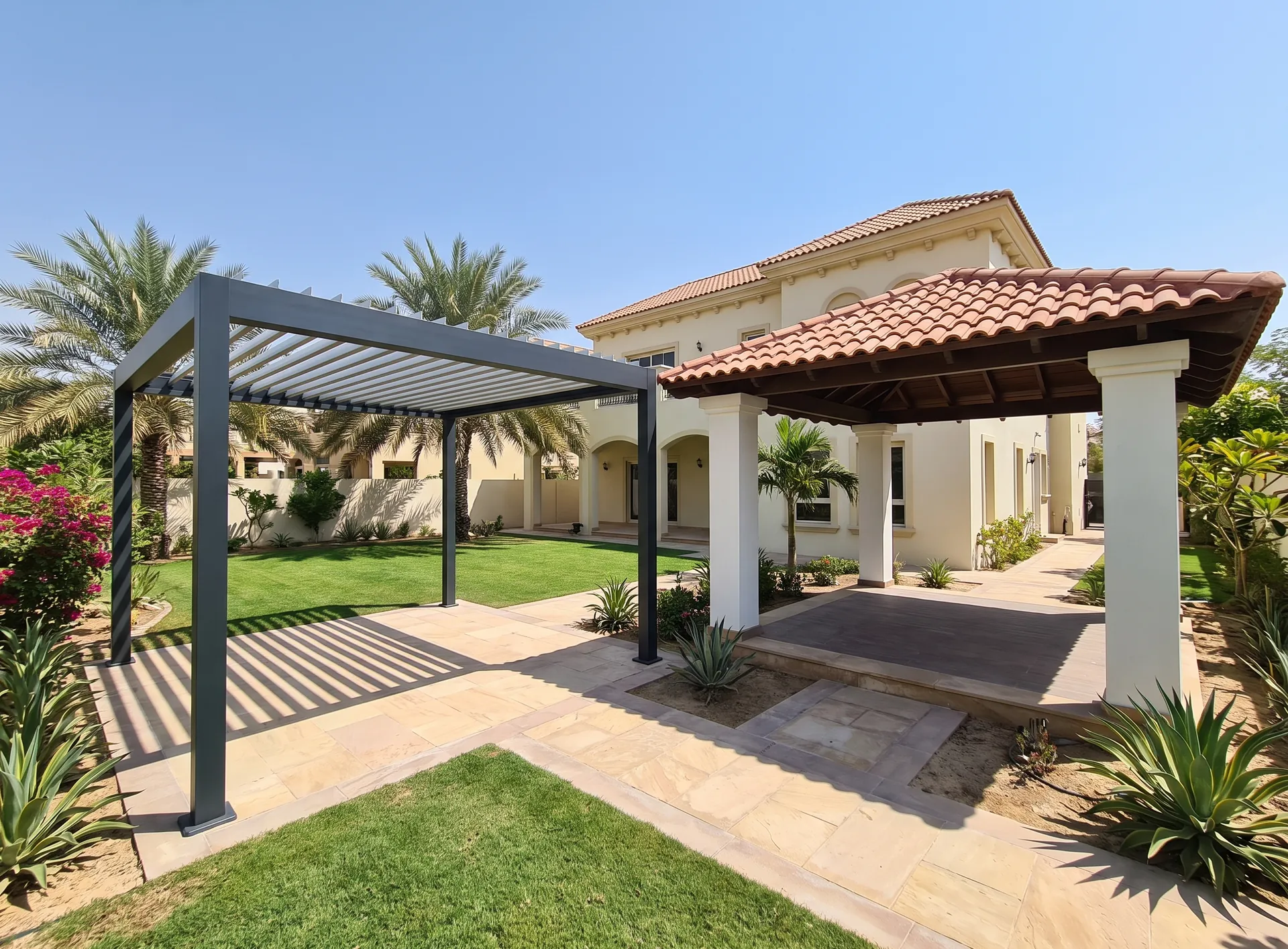 A slim aluminium louvered pergola standing beside a solid-roofed gazebo in a Dubai villa garden, stone paving between them
