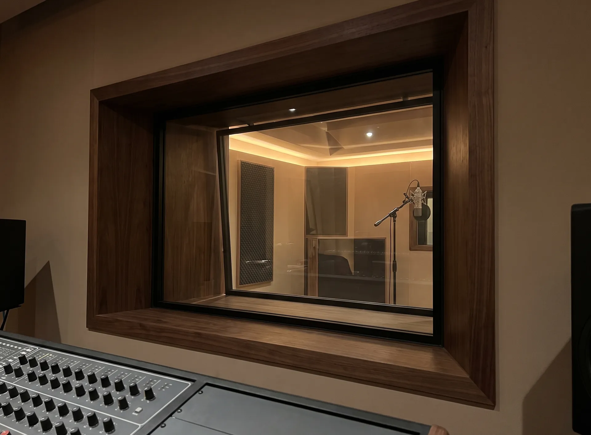 Control room window between a studio live room and control room, two panes of glass set at different angles in a deep timber reveal