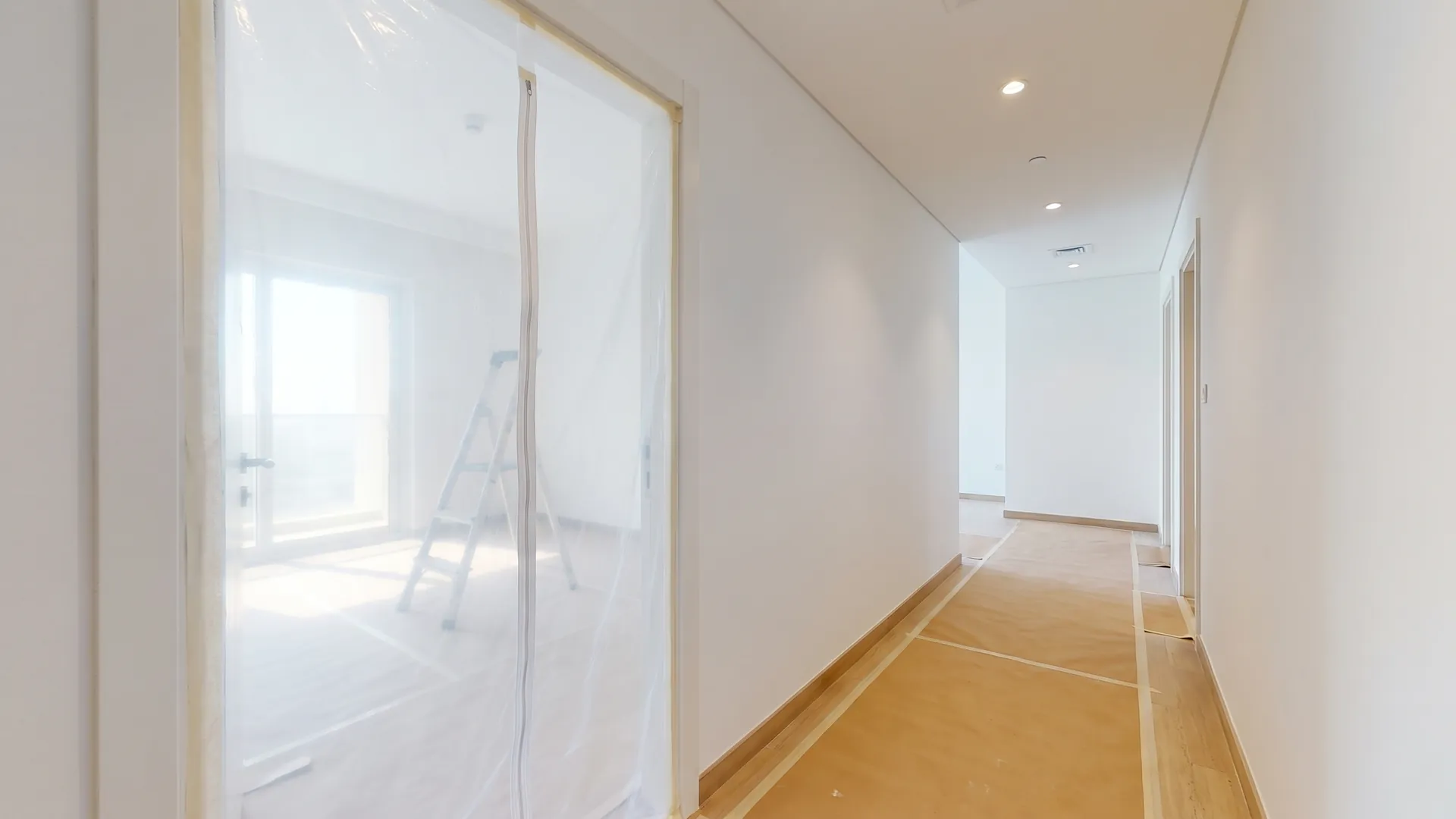 Doorway sealed with a clear plastic dust screen and protective floor covering running along the corridor of an apartment