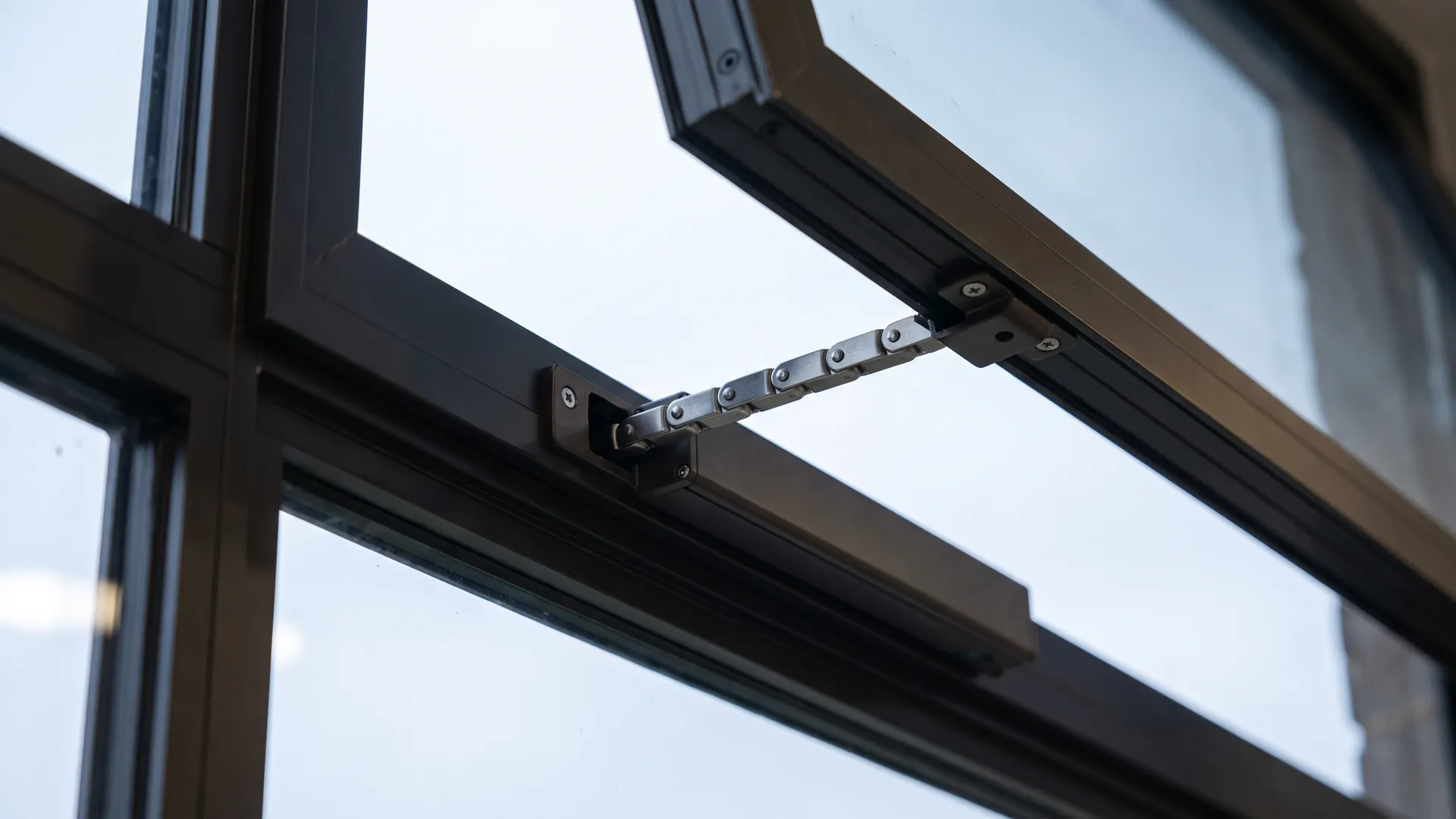 Macro view of a slim chain actuator mounted on a dark anodised aluminium window frame with the chain extended