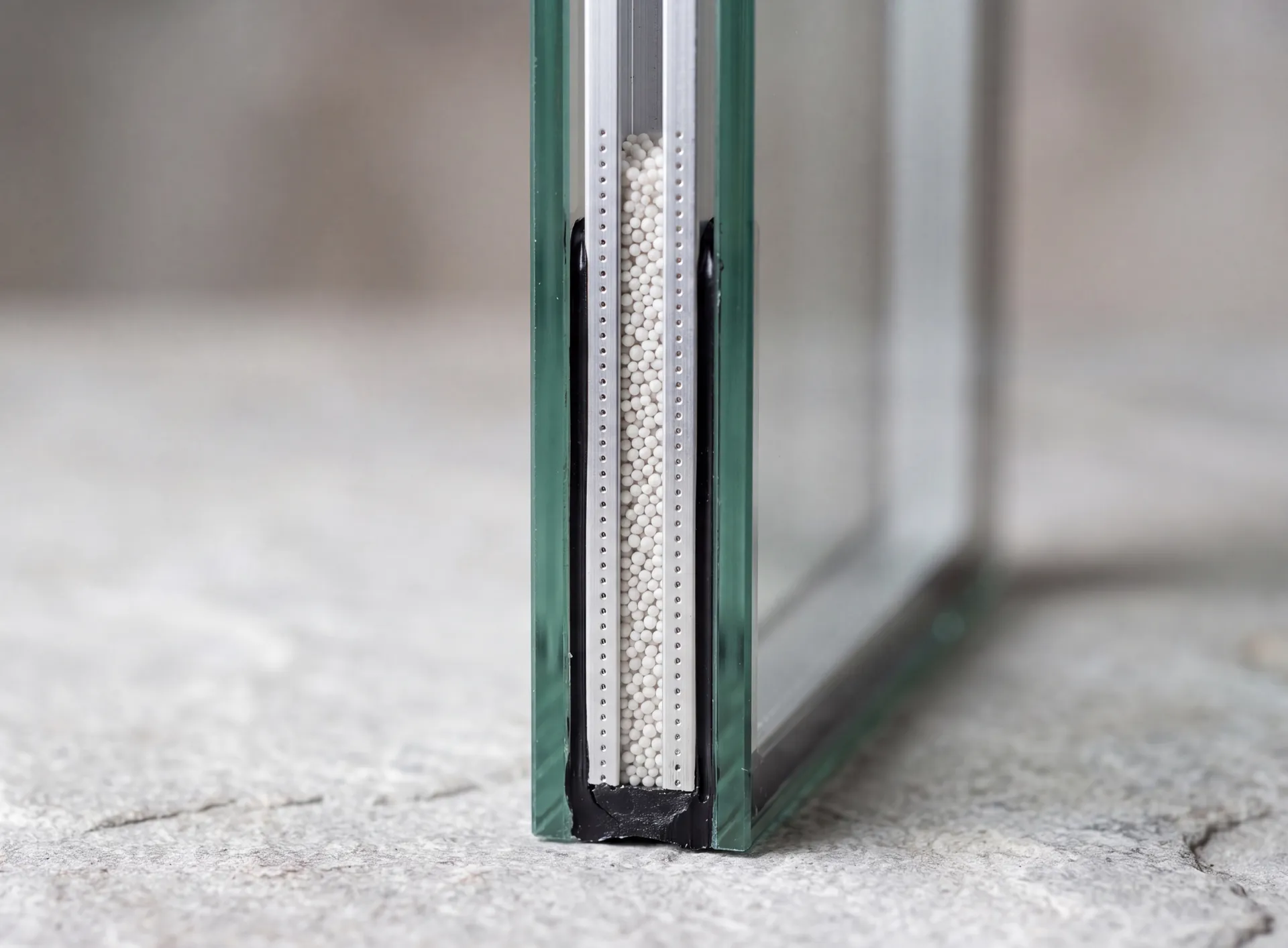 Macro view of the edge of a sealed double glazed unit showing the perforated spacer bar and the black perimeter seal