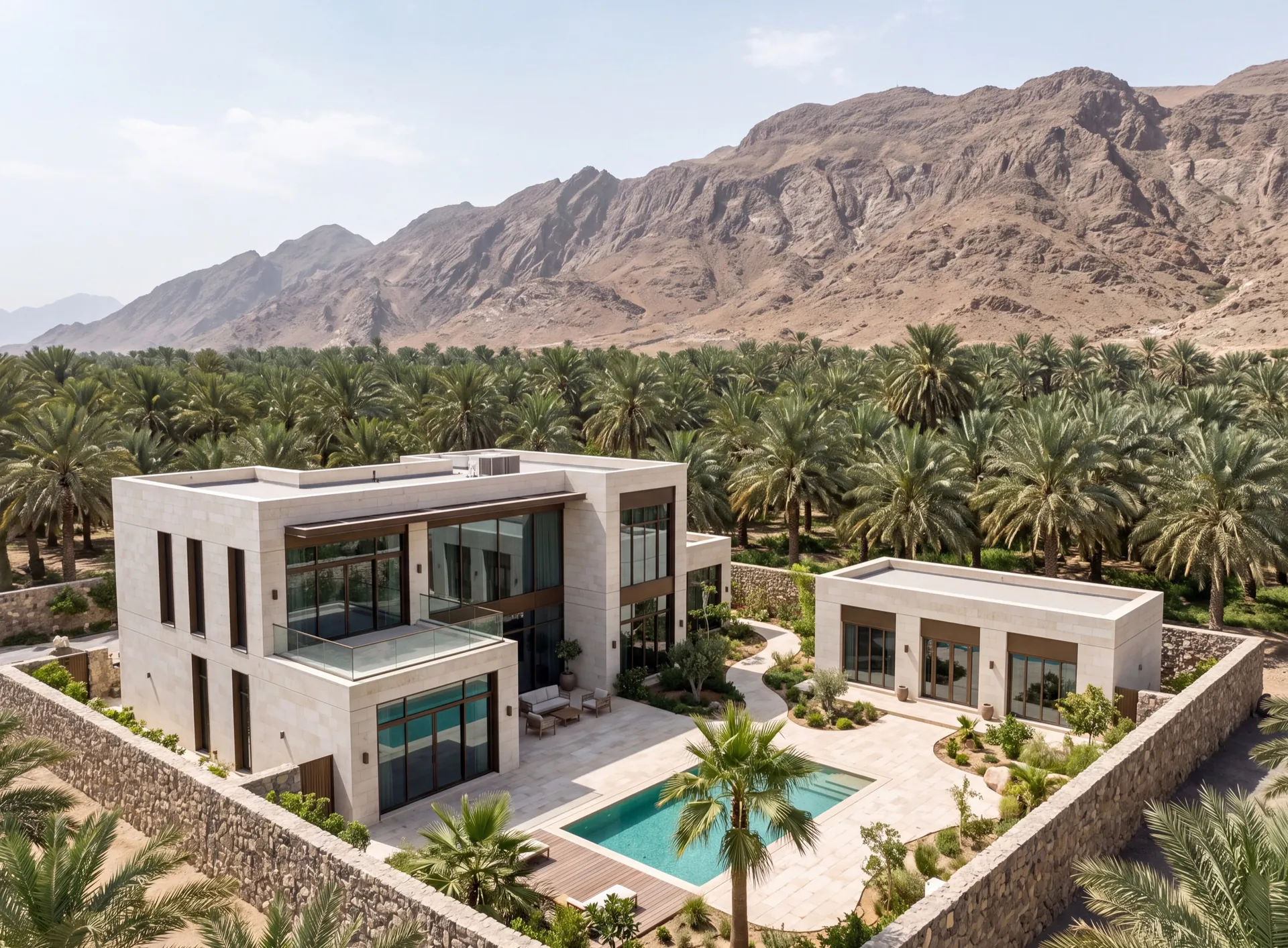 Pale stone family villa in Al Ain with tall bronze-framed aluminium windows, a date palm grove alongside and dry mountains behind